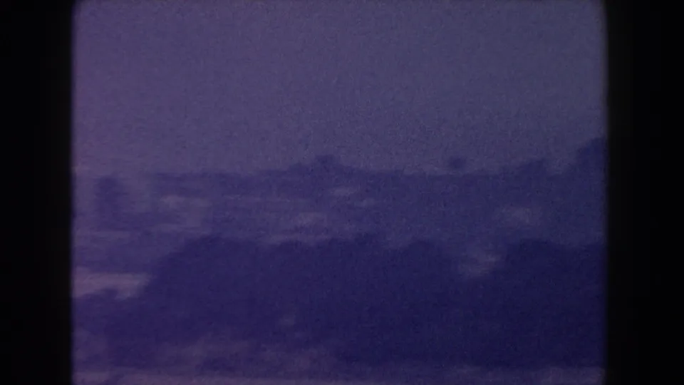 Grainy 8mm view of open water and a blurred distant shoreline, with the scene divided by dark window edges.