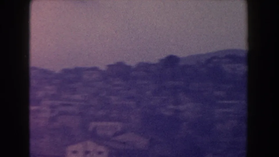1960 Italy 8mm view of a distant hillside settlement, soft and purple-toned with buildings spread across rolling terrain.