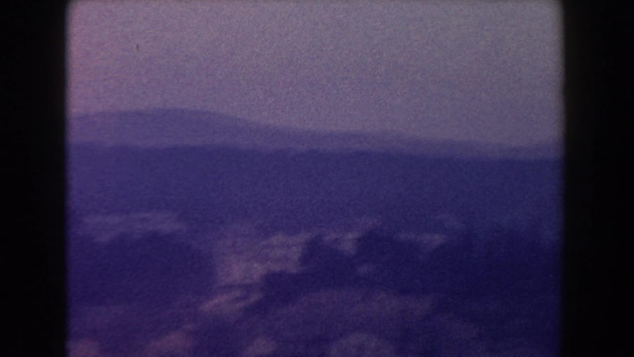 1960 Italy 8mm view of distant mountains and a hillside town under a hazy, muted sky.