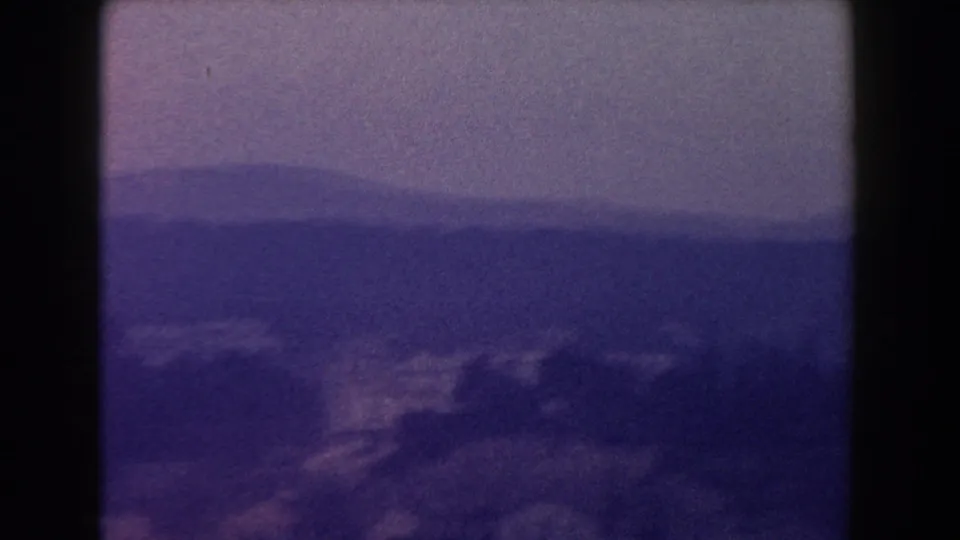 1960 Italy 8mm view of distant mountains and a hillside town under a hazy, muted sky.