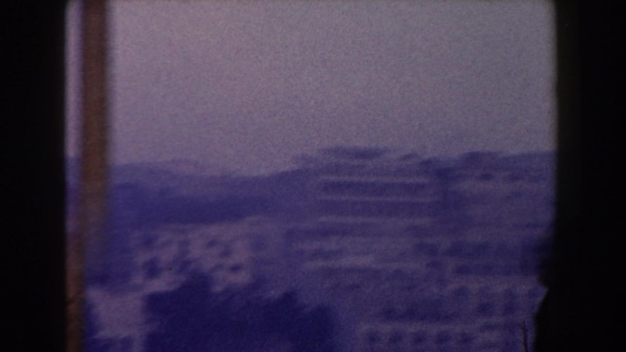 Distant hillside buildings and mountains framed by dark vertical film edges.