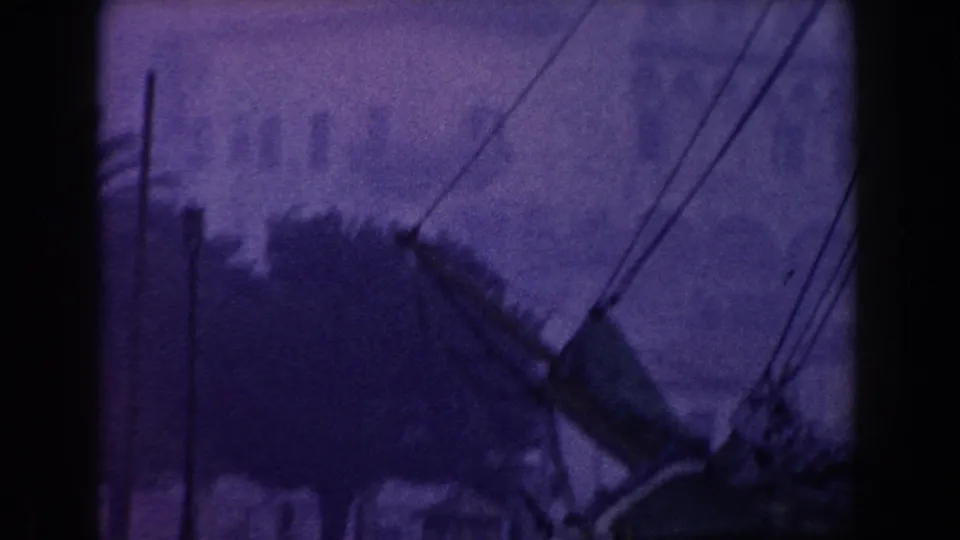 1960 Italy 8mm town view with overhead utility lines, rooftops, trees, and hazy buildings.