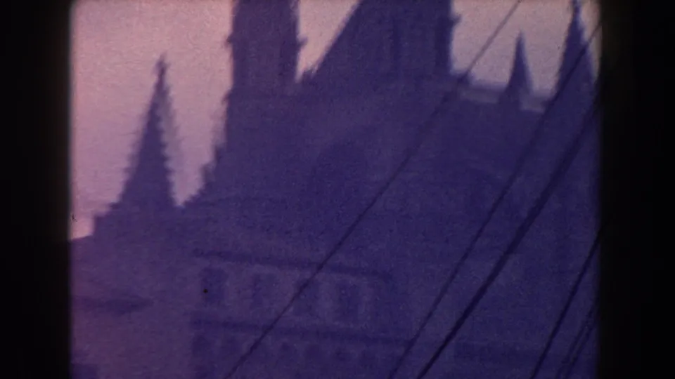 1960 Italy 8mm frame showing a church spire, rooftops, trees, and overhead wires in haze.