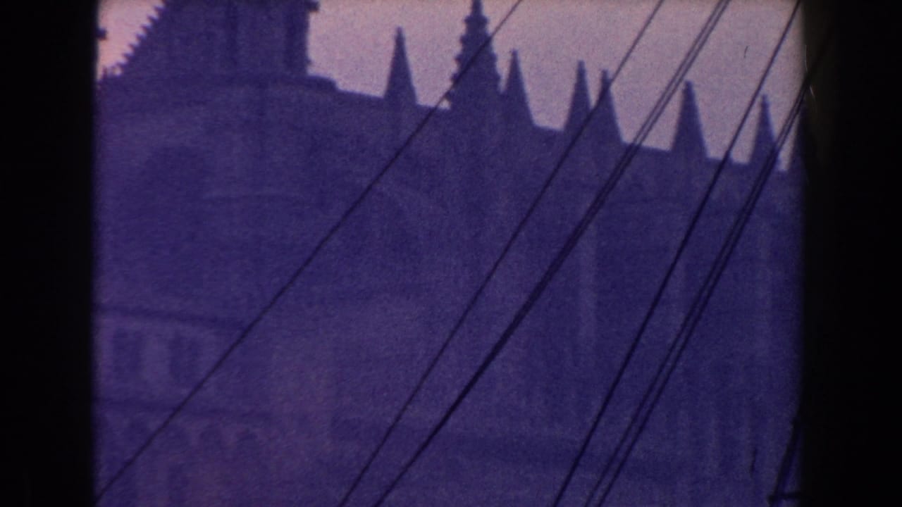 1960 Italy 8mm view of coastal town architecture and a spire-like roofline seen through dark framing and ship cables.