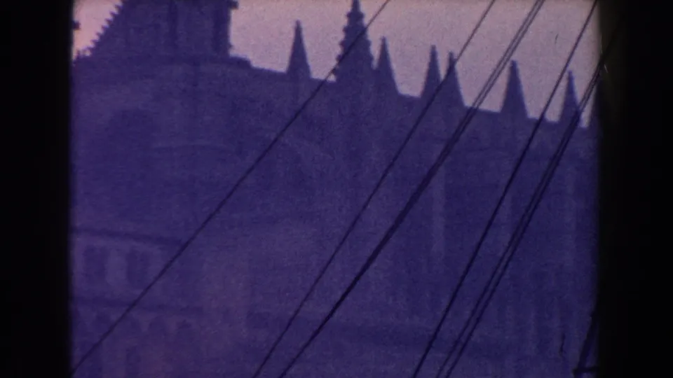 1960 Italy 8mm view of coastal town architecture and a spire-like roofline seen through dark framing and ship cables.
