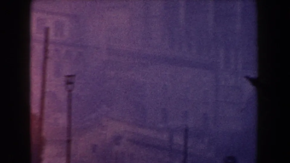 1960 Italy 8mm frame showing hazy shoreline architecture beyond dark ship-edge framing and faint vertical posts.