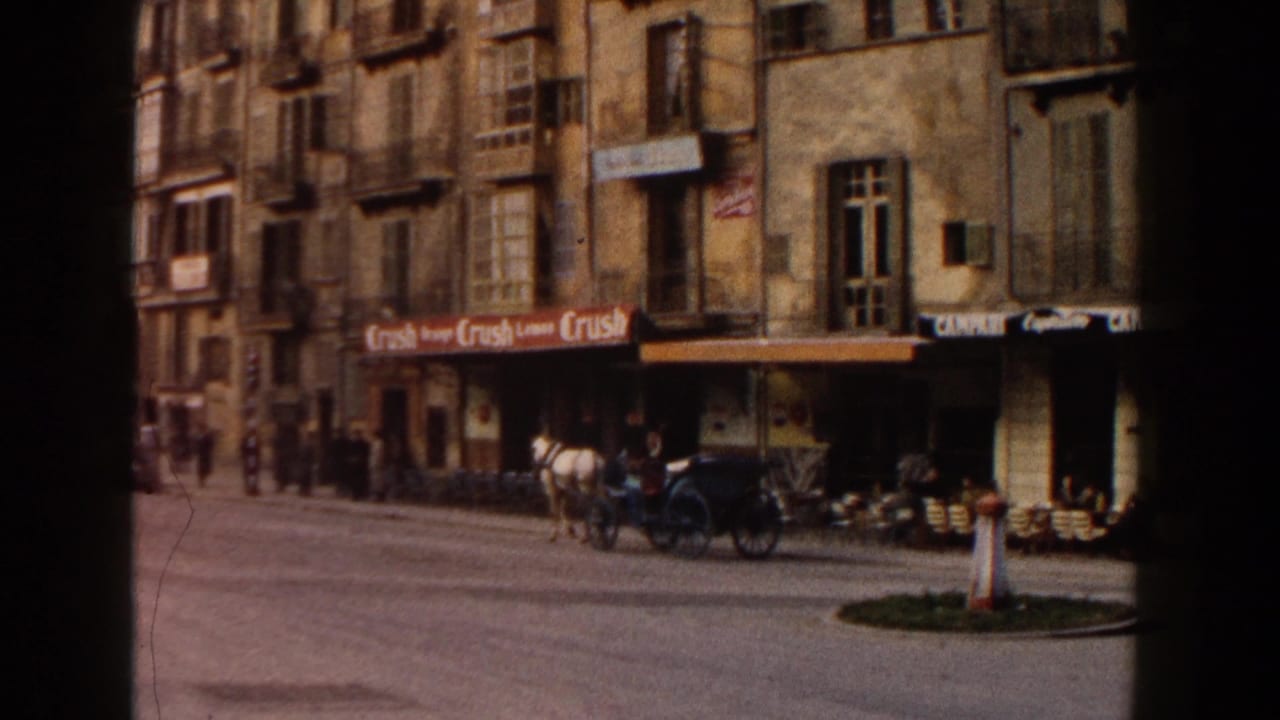 1960 Italy home-movie frame showing a horse-drawn carriage, cafe frontage, pedestrians, and older apartment buildings along a city street.