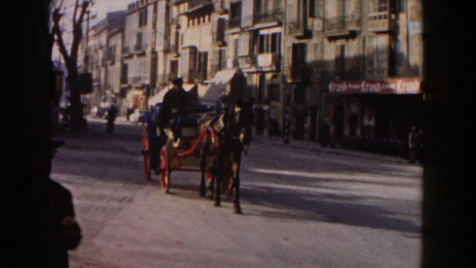1960 Italy street view with an animal-drawn cart in the foreground, pedestrians along the sidewalks, storefront signage, and mid-century traffic.