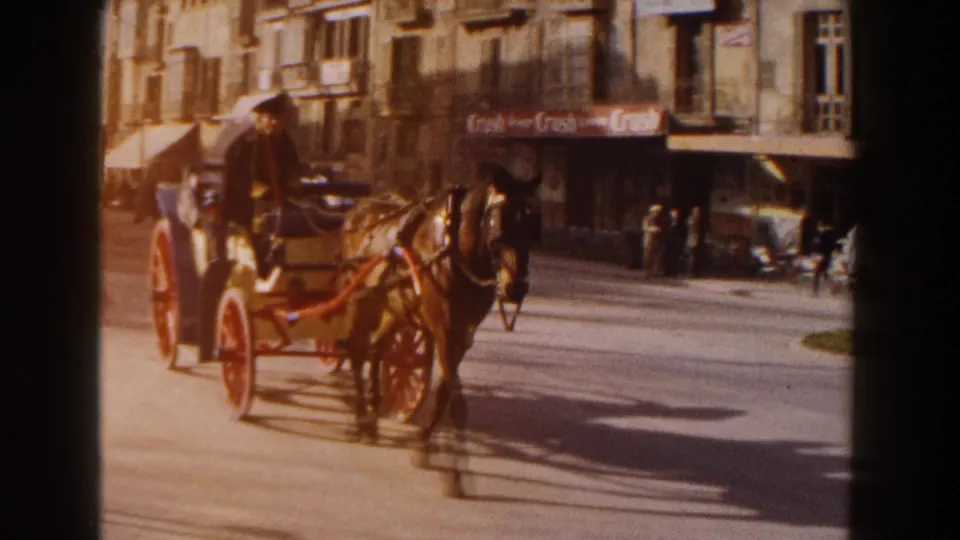 The carriage passes closer to the camera on a 1960 Italy street, with a dark horse, red wheels, shopfronts and pedestrians visible.
