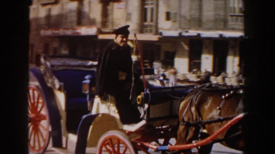 Near the end of the clip, the driver and front of the horse-drawn carriage fill the frame against a row of European storefronts.