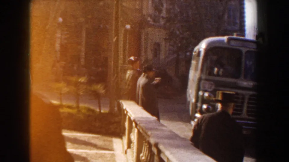 A caped buggy driver appears near the curb as a green bus occupies the right side of the 1960 Italy frame.