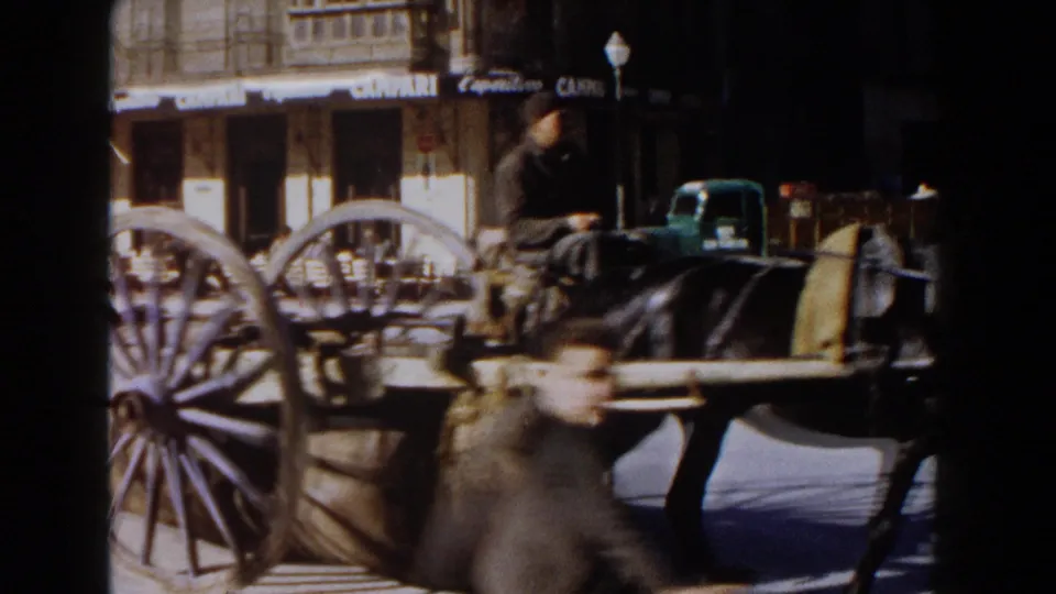 Close view of a horse-drawn cart in an Italian square, with a blurred pedestrian crossing foreground and café signs behind.