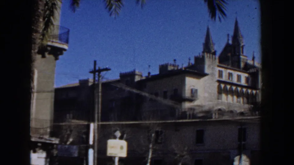 A 1960 Italy travel view shows a historic building with pointed spires, street poles, palm fronds, and nearby rooftops.