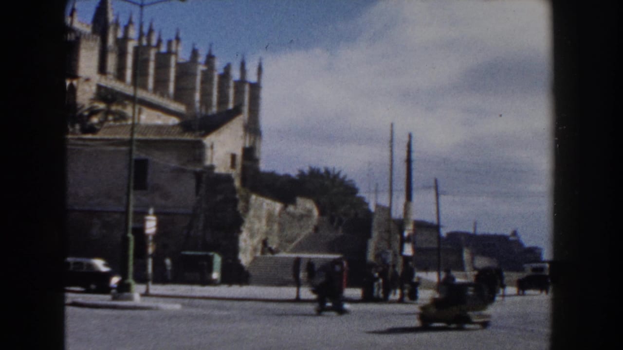 1960 Italy street view with a Gothic-style building at left, light traffic, pedestrians, and utility poles seen through a dark film frame.