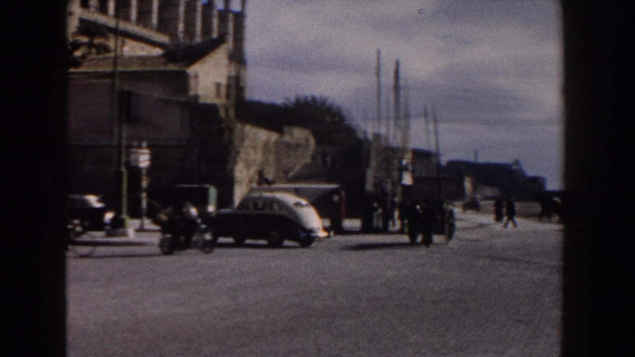 1960 Italy street view with a classic car, a motorbike, pedestrians, signs, stone architecture, and open paved roadway.