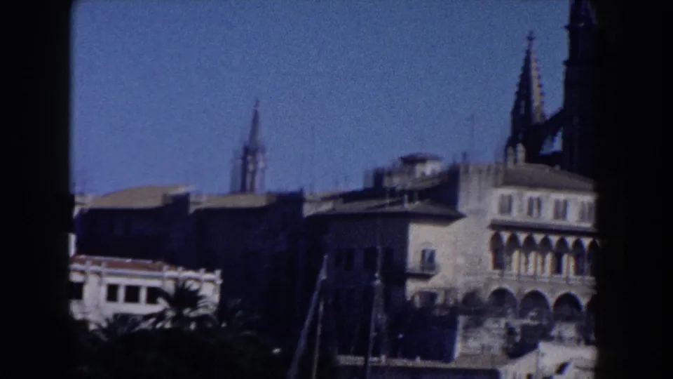 1960 Italy 8mm frame showing a large Gothic-style church structure with spires, arcades, and nearby rooftops.