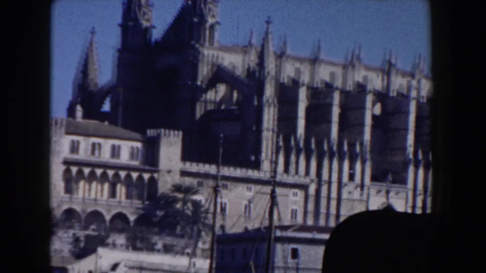 1960 Italy 8mm frame of a large Gothic-style church facade with spires, stone arcades, and foreground shadow.