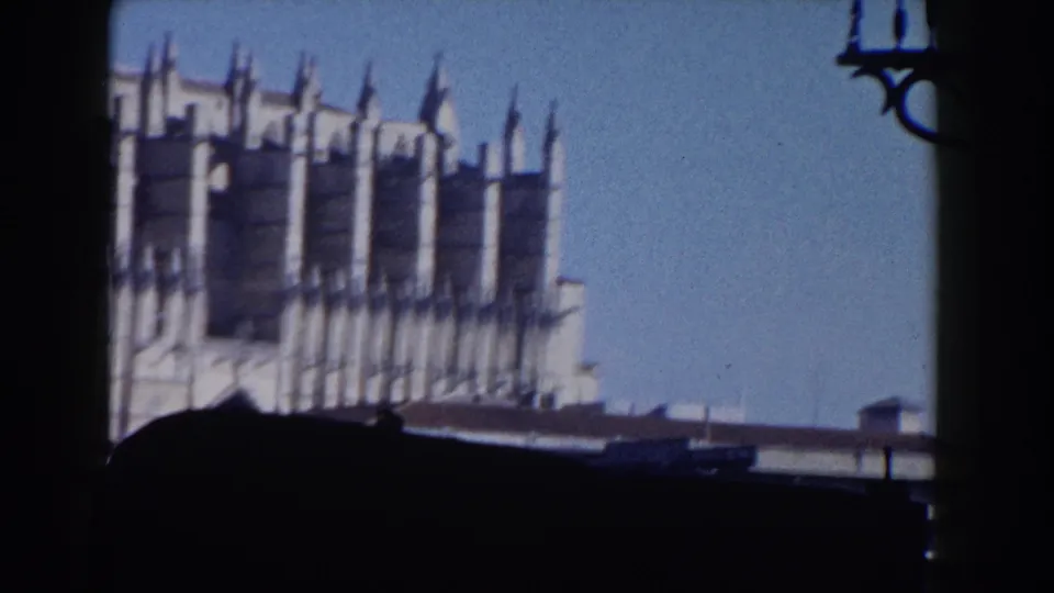 1960 Italy home-movie frame showing the cathedral's upper Gothic facade, with strong shadowed foreground obstruction and blue sky beyond.
