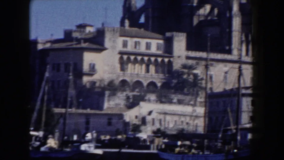 1960 Italy 8mm view of waterfront buildings, boat masts, palm foliage, and the edge of a Gothic cathedral facade.