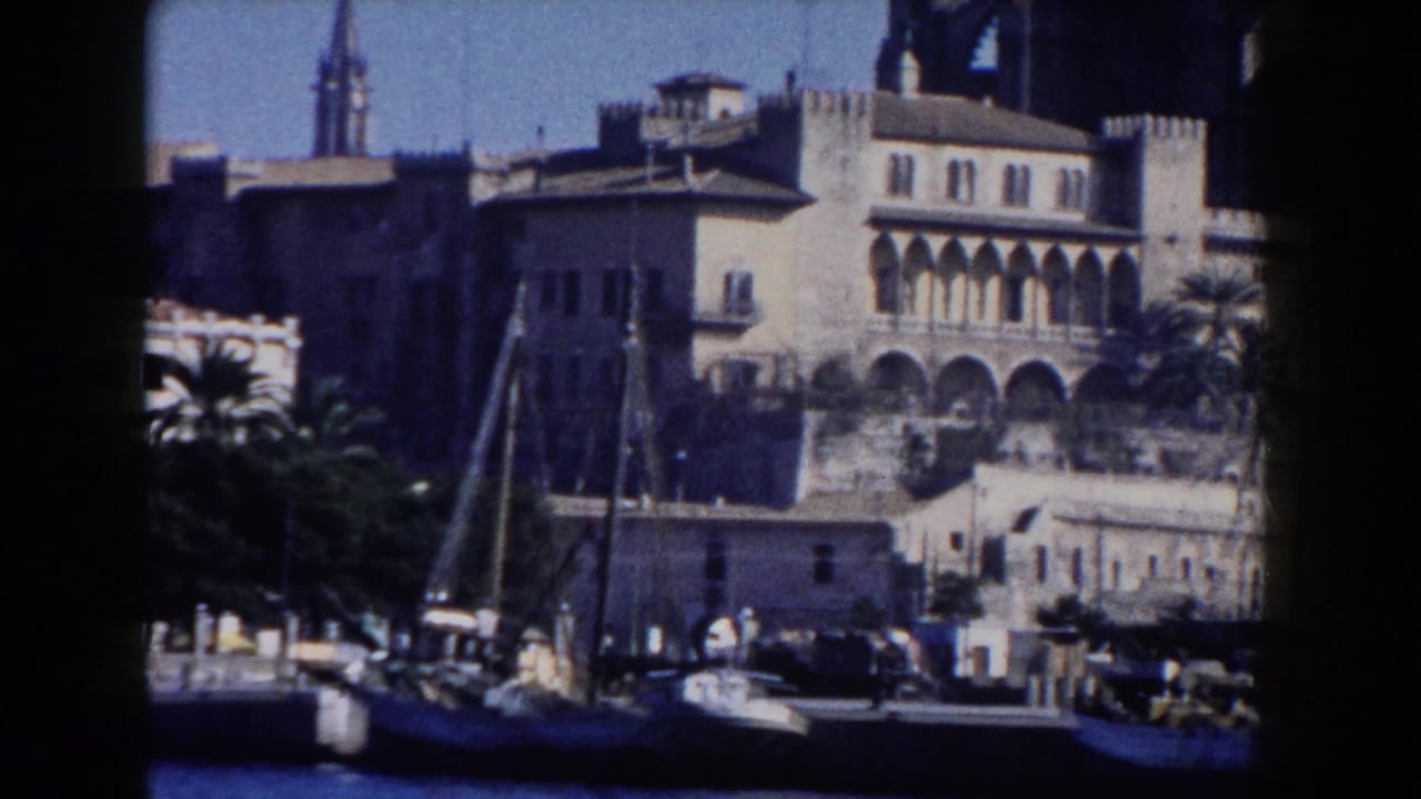 1960 Italy 8mm view of waterfront buildings with arches, a church spire, palm trees, water, and small boats.