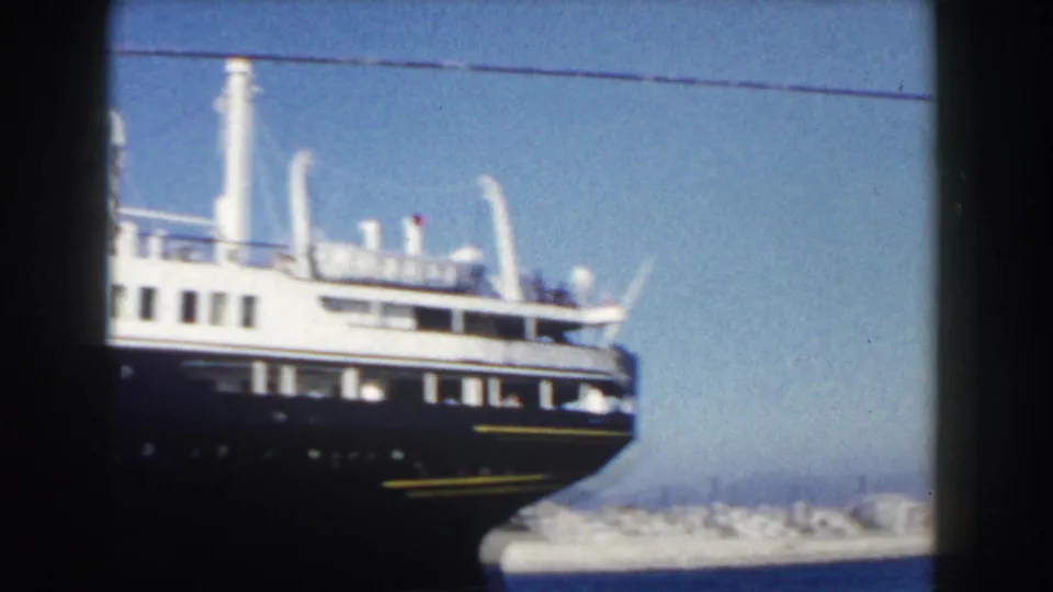 Large white passenger ship at an Italian port in 1960, partly framed by dark foreground railings and open sky.