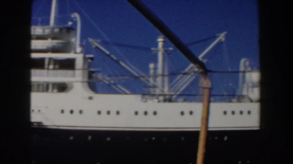 Close 8mm view of the passenger ship's upper decks, rigging, windows, and white hull against a blue sky in Italy.
