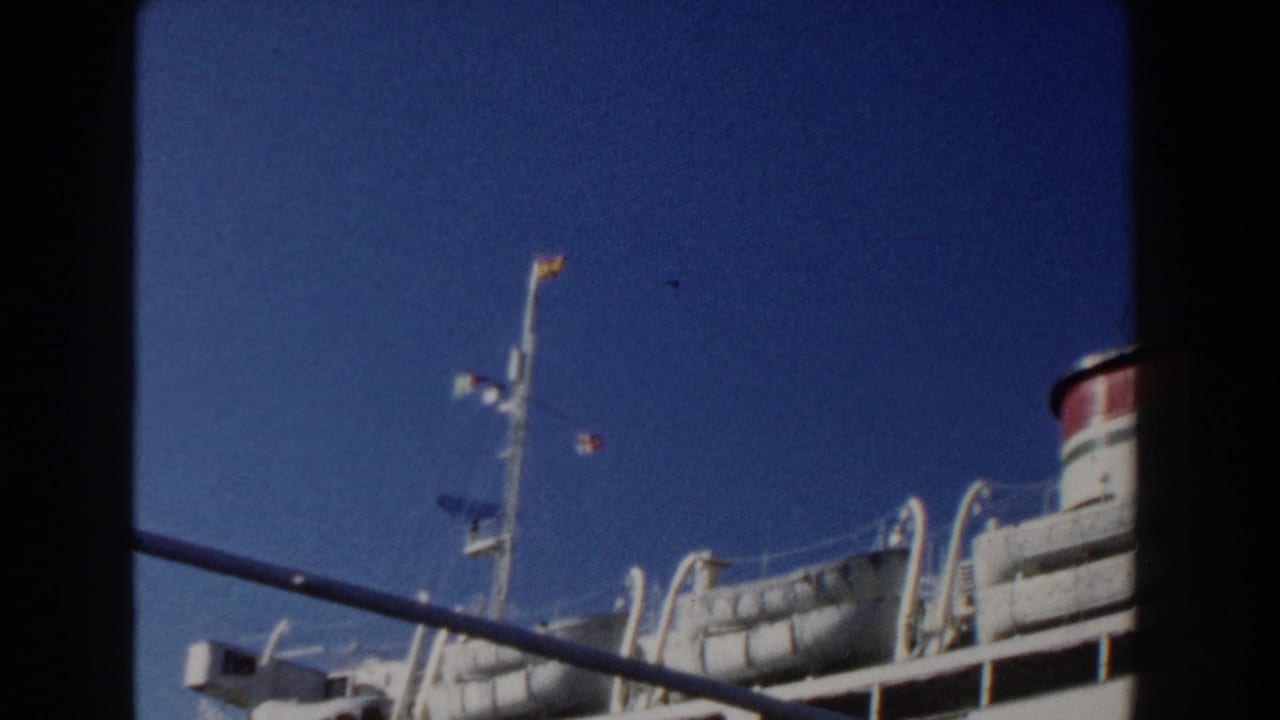 1960 Italy 8mm frame showing a white ocean liner with upper decks and lifeboats viewed from a nearby vessel.