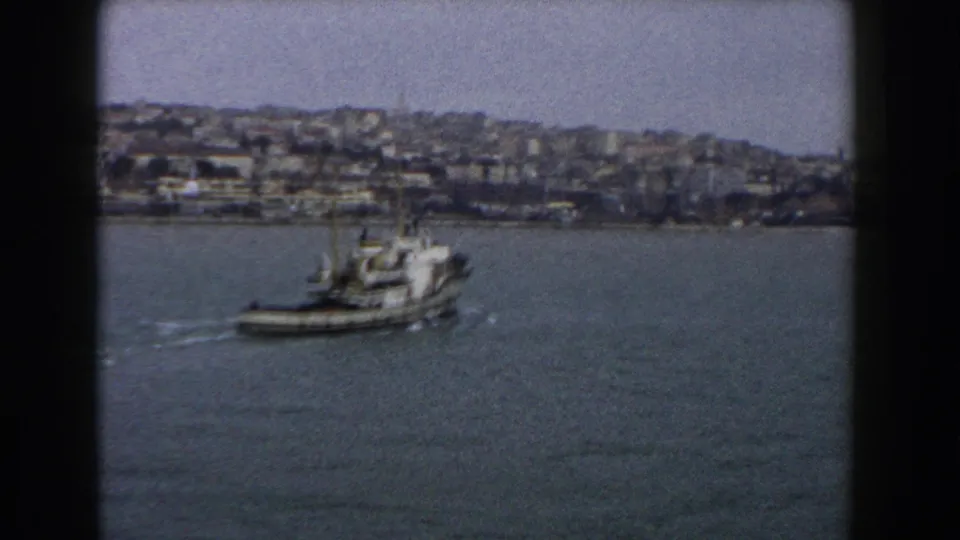 A small boat appears farther across the harbor water, framed by dark 8mm edges and a distant Italian hillside waterfront.