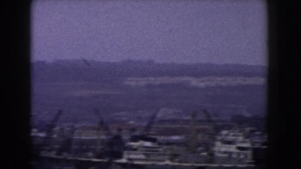 1960 8mm Italian town view with clustered buildings, construction cranes, and a muted hillside skyline.