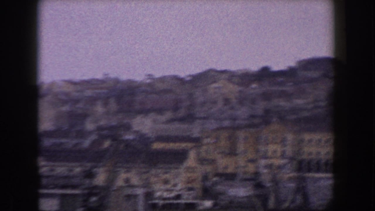 1960 8mm view of an Italian waterfront town and hillside, filmed from a moving boat through a dark frame edge.