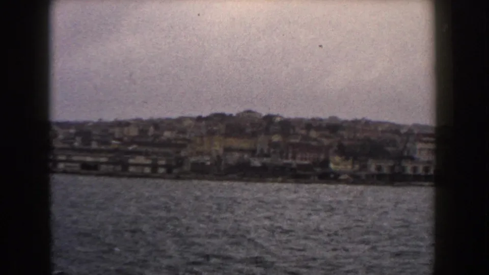 Italian waterfront buildings and a hillside town appear across the water in a soft 1960 home-movie frame.