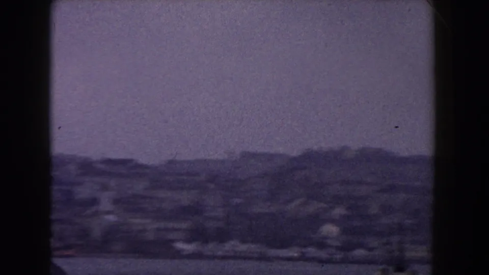 Distant Italian shoreline and hillside buildings appear softened by grain, haze, and purple-tinted 8mm color shift.