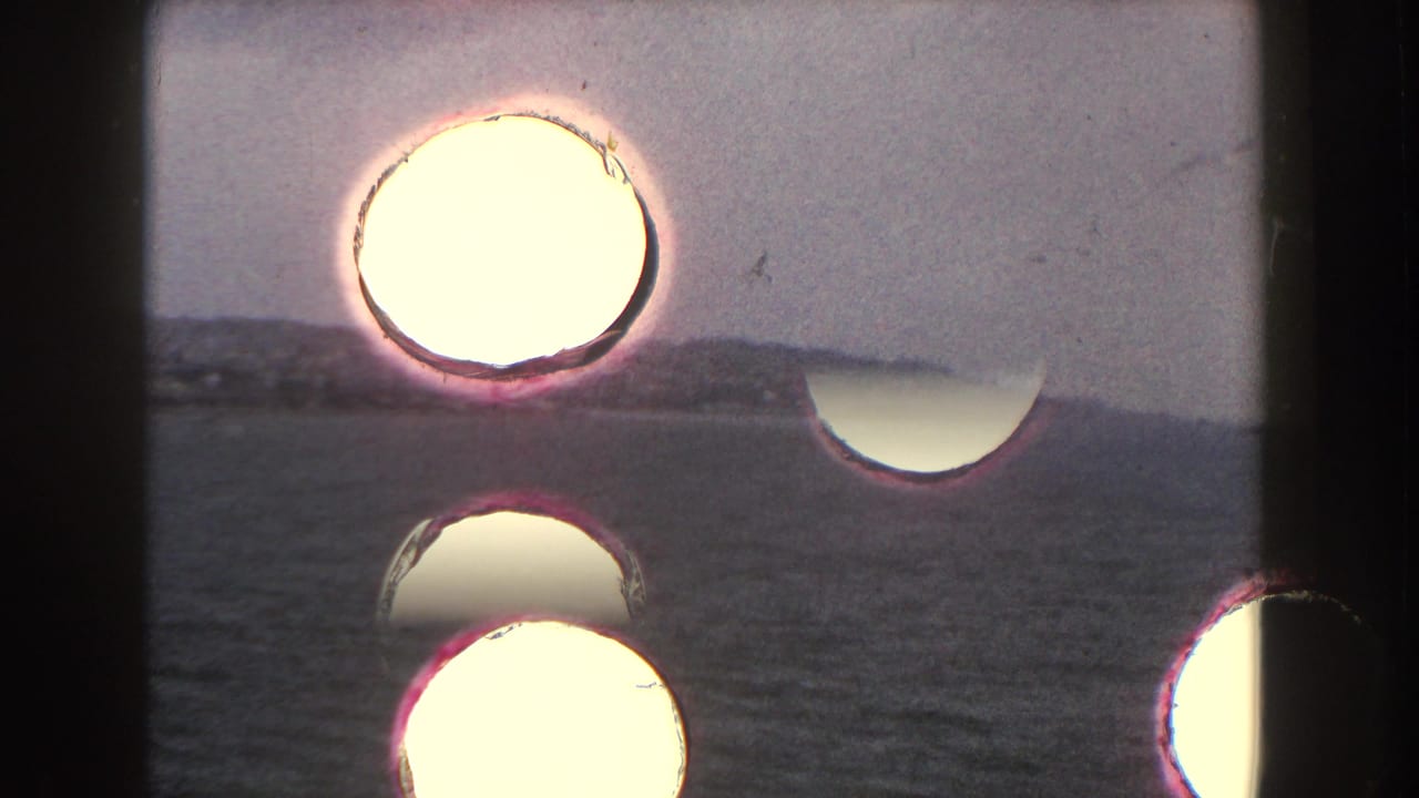Coastal water and distant shoreline seen behind dark framing and bright circular film marks.