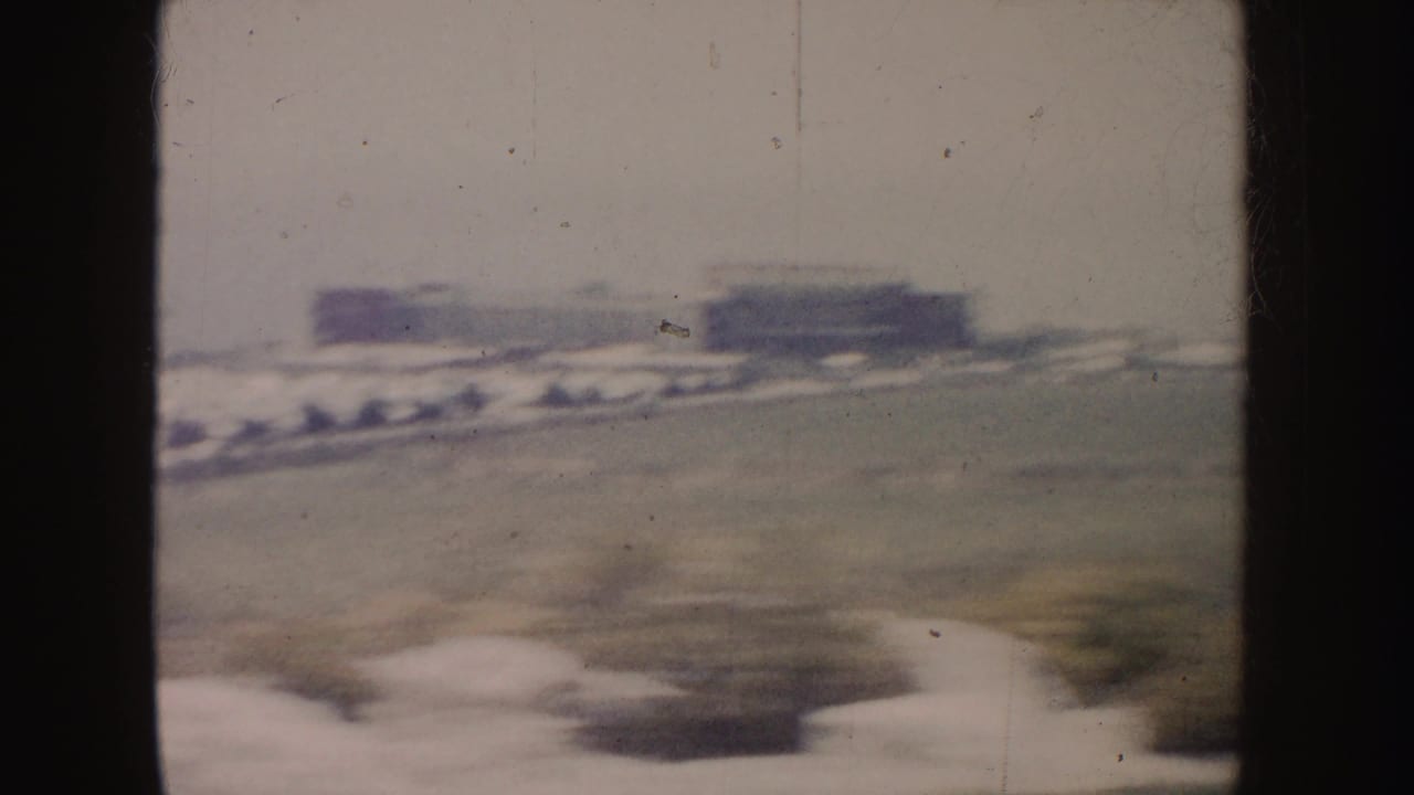 Blurred roadside view with distant low buildings and a car passing in the foreground.