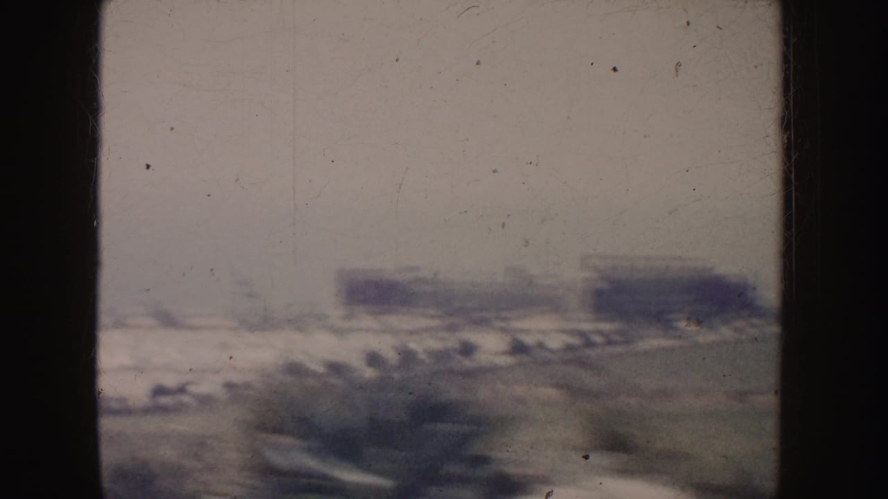 Blurry urban roadside with parked or moving vehicles and low buildings in the distance.