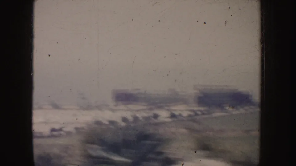 Hazy 1962 California roadway view with indistinct vehicles, low buildings, roadside vegetation, and heavy motion blur.