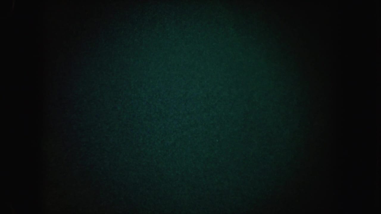 Nearly black underexposed frame with green grain and a dim light area near the center.