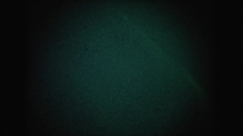 1962 California 8mm darkness frame with a broader greenish light patch, heavy grain, and no identifiable subject.
