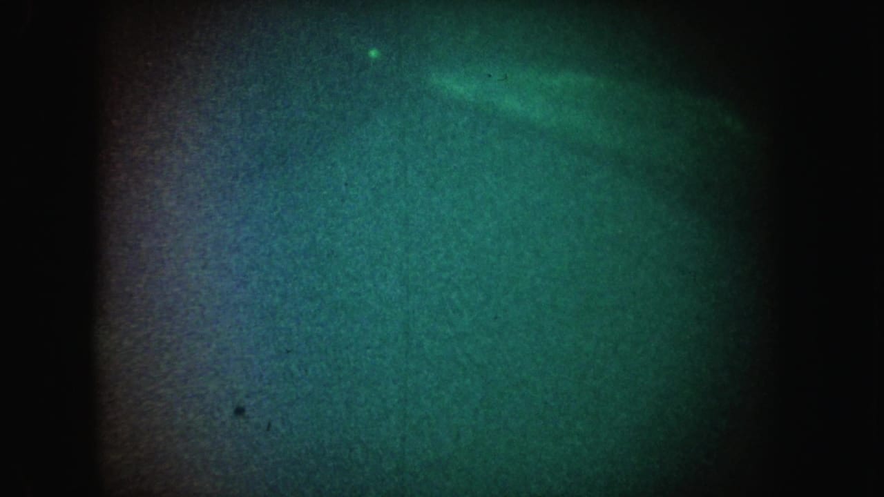 1962 California 8mm frame with a dim green-blue underwater-looking field, heavy grain, and a small bright speck near the top.