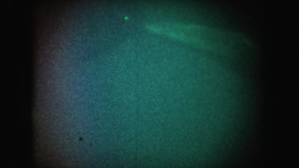1962 California 8mm frame with a dim green-blue underwater-looking field, heavy grain, and a small bright speck near the top.