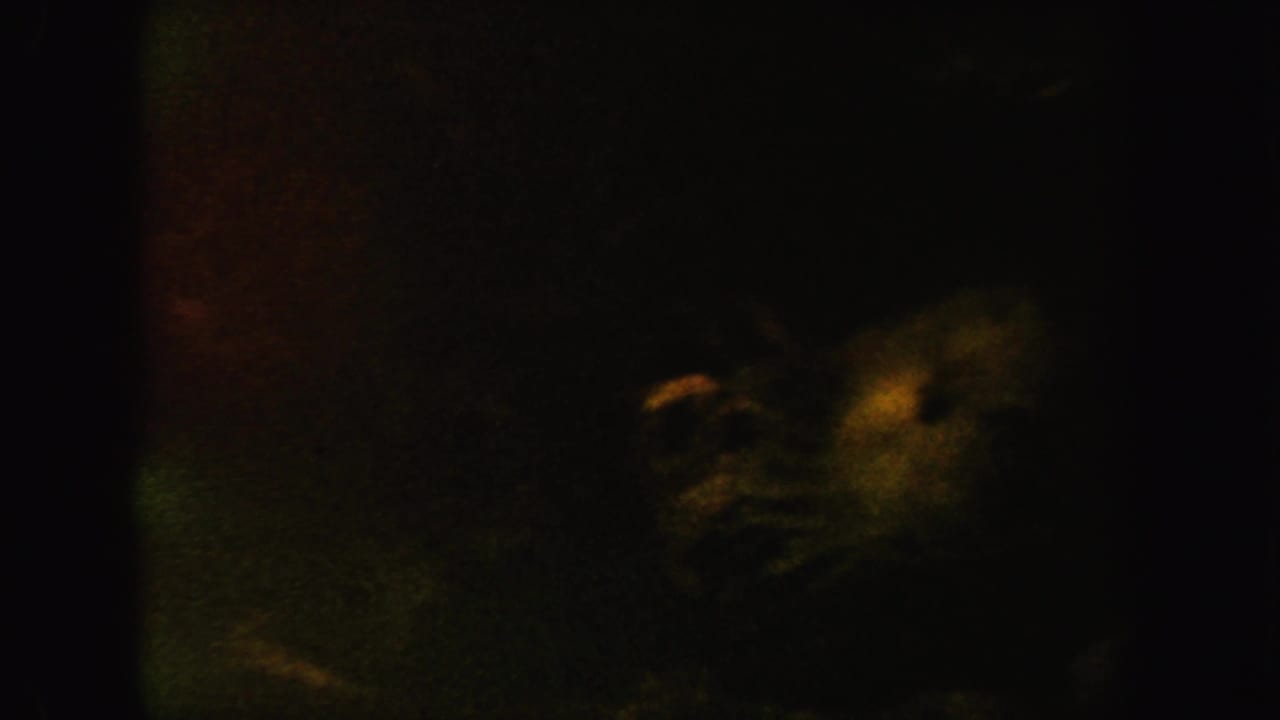 Dark murky frame with faint green and amber underwater shapes near the right side.