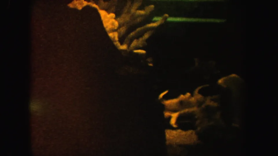1962 California 8mm frame shows a dim cave-like scene partly obscured by a dark vertical band, with bone-like shapes and warm highlights.