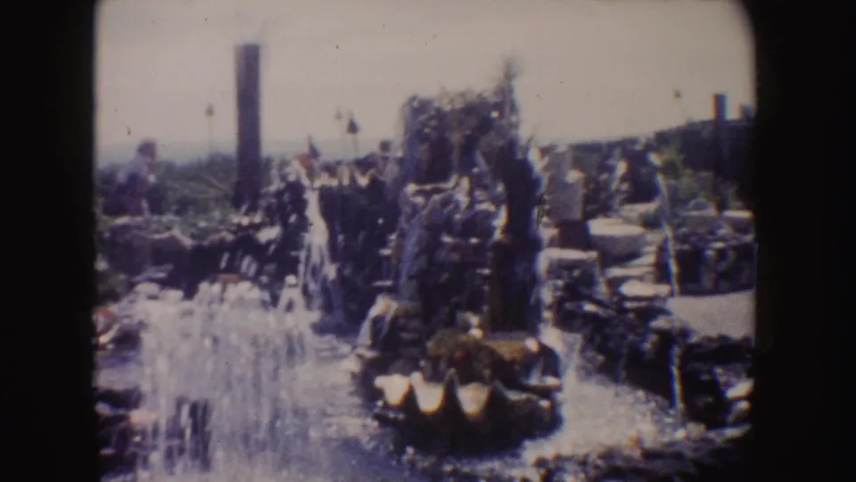 1962 California home-movie frame showing a rocky coastal garden with plants, a water feature, and bright sun exposure.