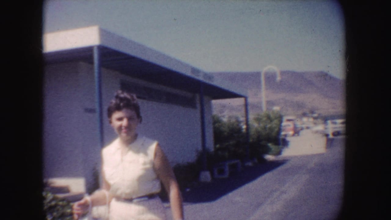 Woman in a white sleeveless dress walking near a low building and paved path.