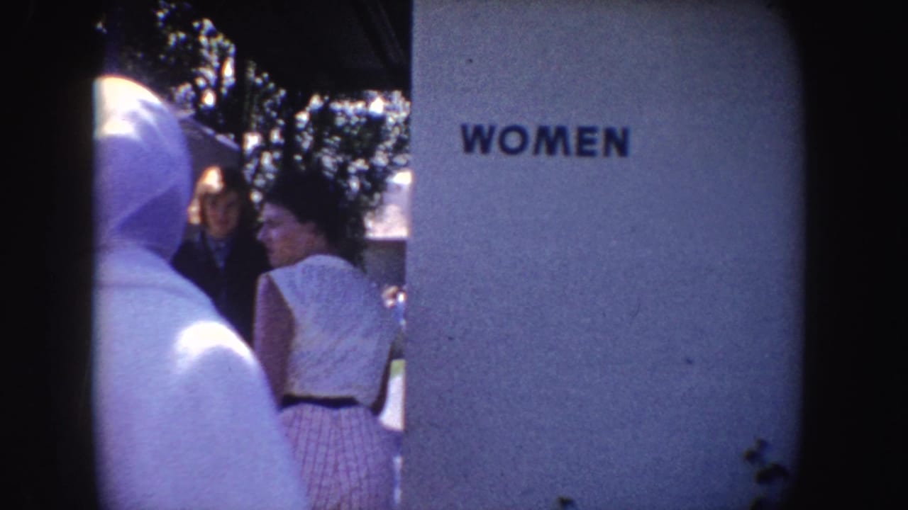 1962 California home-movie frame showing spectators near a WOMEN restroom sign at a water-park or dolphin-show setting.