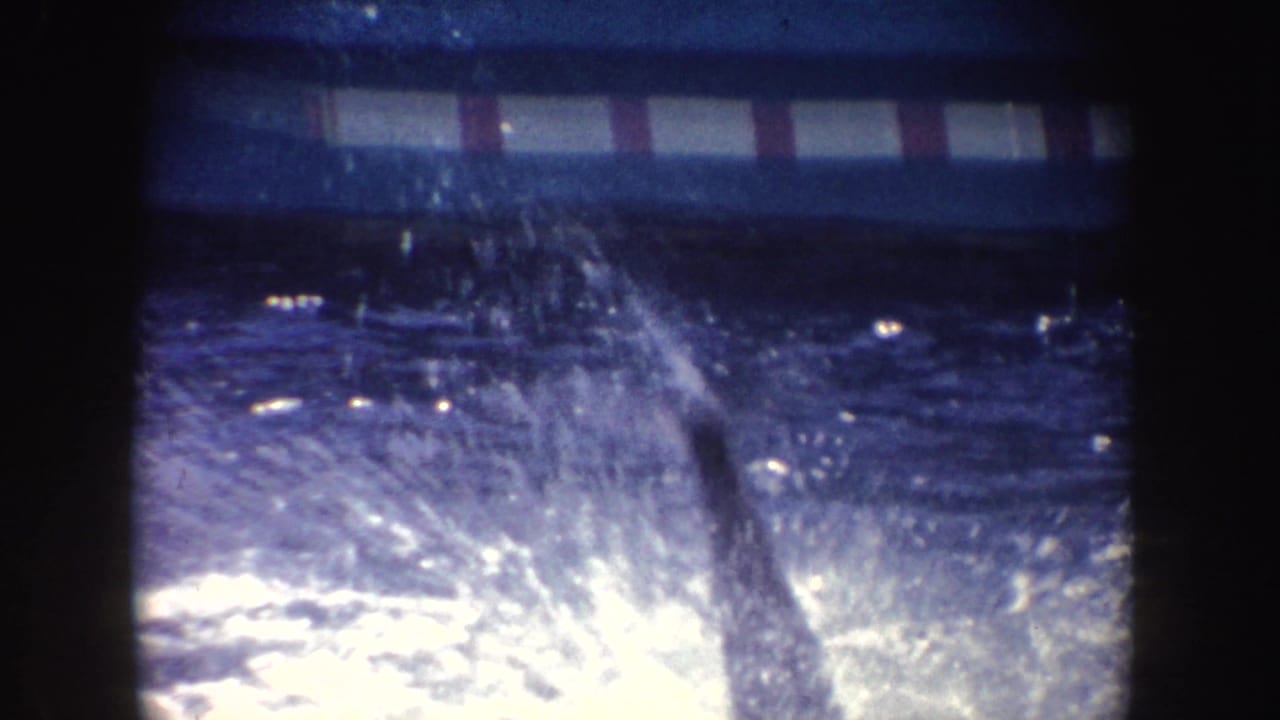 Water splashes in a pool behind a red-and-white striped barrier.