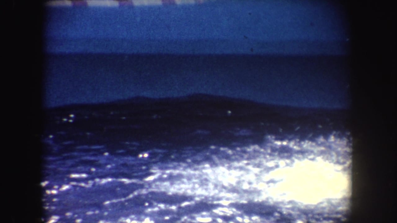 1962 California 8mm frame showing dark water sparkling behind a low viewing barrier, with no clear people in this frame.