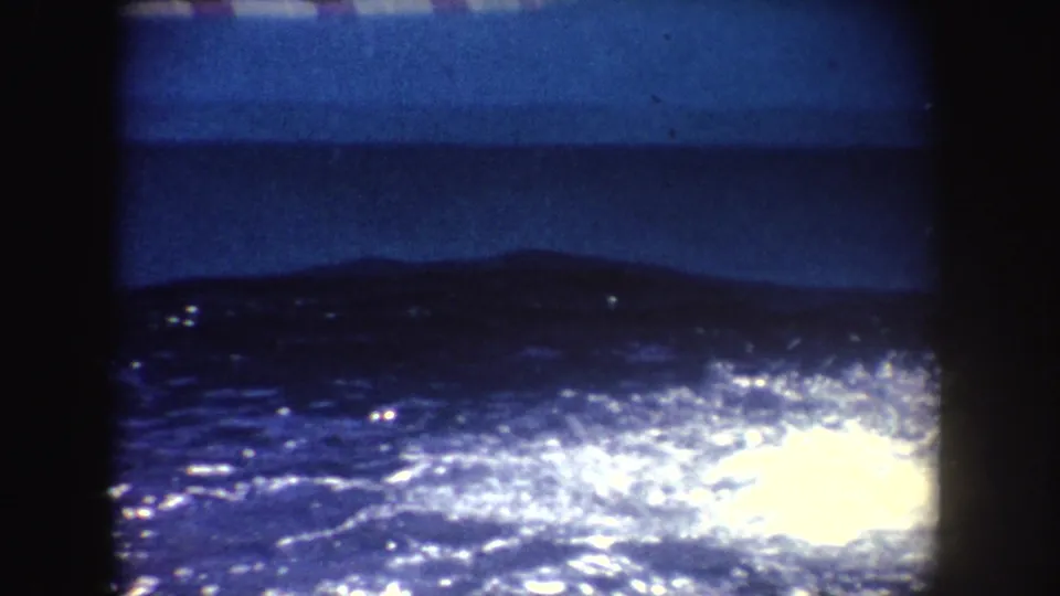 1962 California 8mm frame showing dark water sparkling behind a low viewing barrier, with no clear people in this frame.