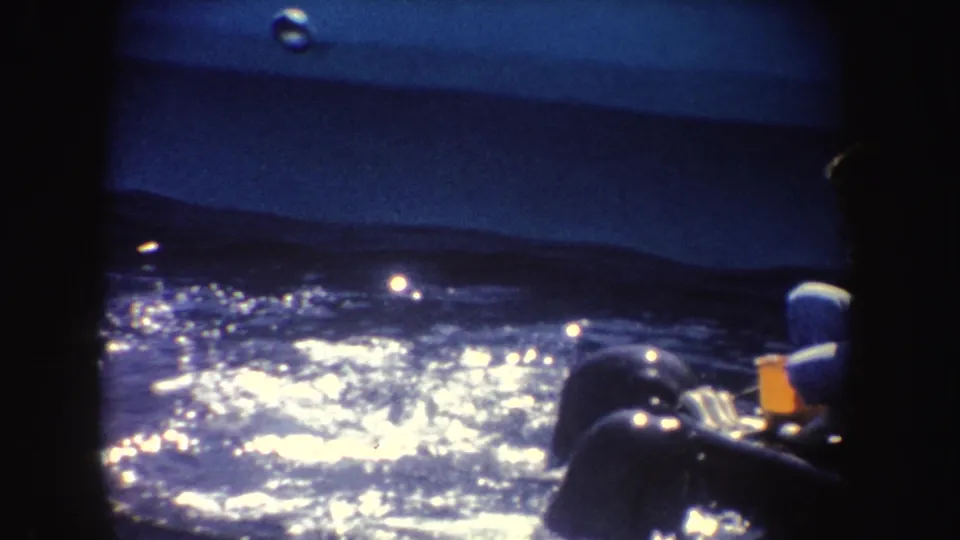 1962 California 8mm frame showing reflective dark water, a barrier, and the partial figure of a spectator at the right edge.