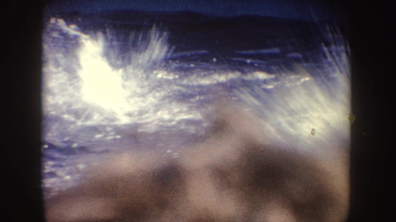1962 California 8mm frame with bright water glare, blue pool tones, and a blurred foreground obstruction within dark film borders.
